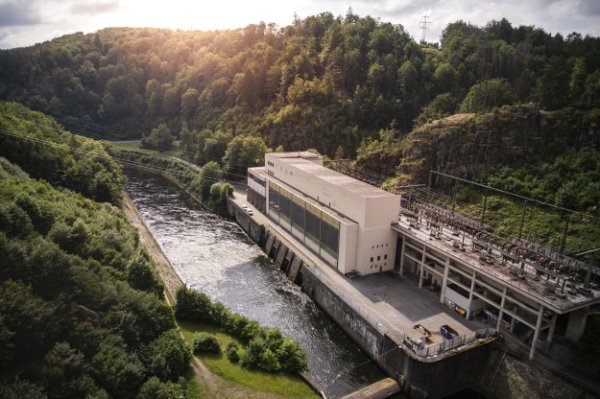 Wasserkraftwerk an einem Fluss mit bewaldeten Hügeln im Hintergrund, Österreich